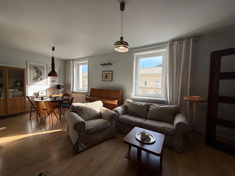 Nowoczesny salon z beżową kanapą, fotelem, stołem i wiszącymi lampami, ściany po malowaniu, podłoga po układaniu paneli