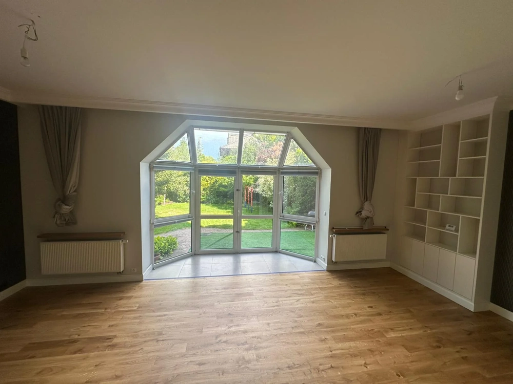 Salon z podłogą z paneli, białymi ścianami, wnęką okienną i zabudowanym regałem Układanie paneli