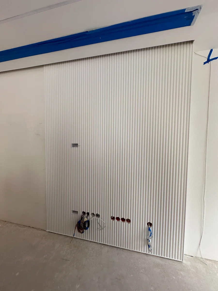 Zabudowa ściany z płyt GK z pionowym ryflowaniem i otworami na kable elektryczne