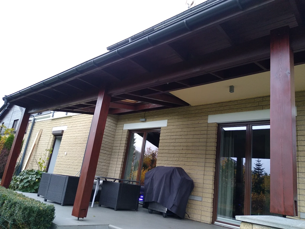 Zadaszony taras z drewnianymi słupami i widoczną rynną na krawędzi dachu – montaż rynien