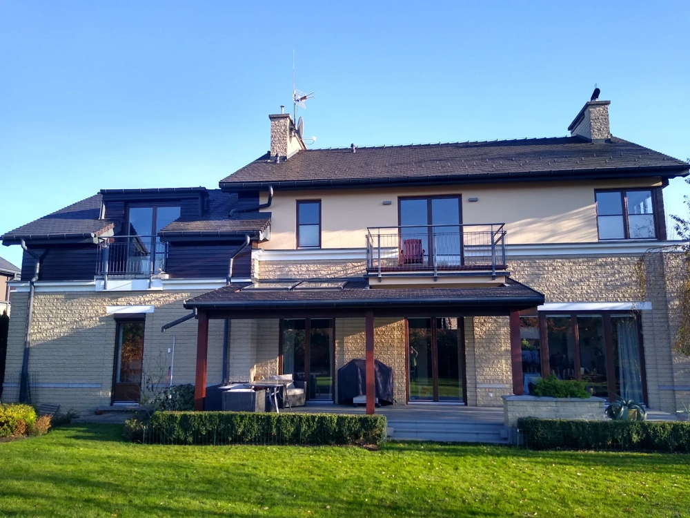 Montaż rynien na dachu nowoczesnego domu z kamienną elewacją i tarasem