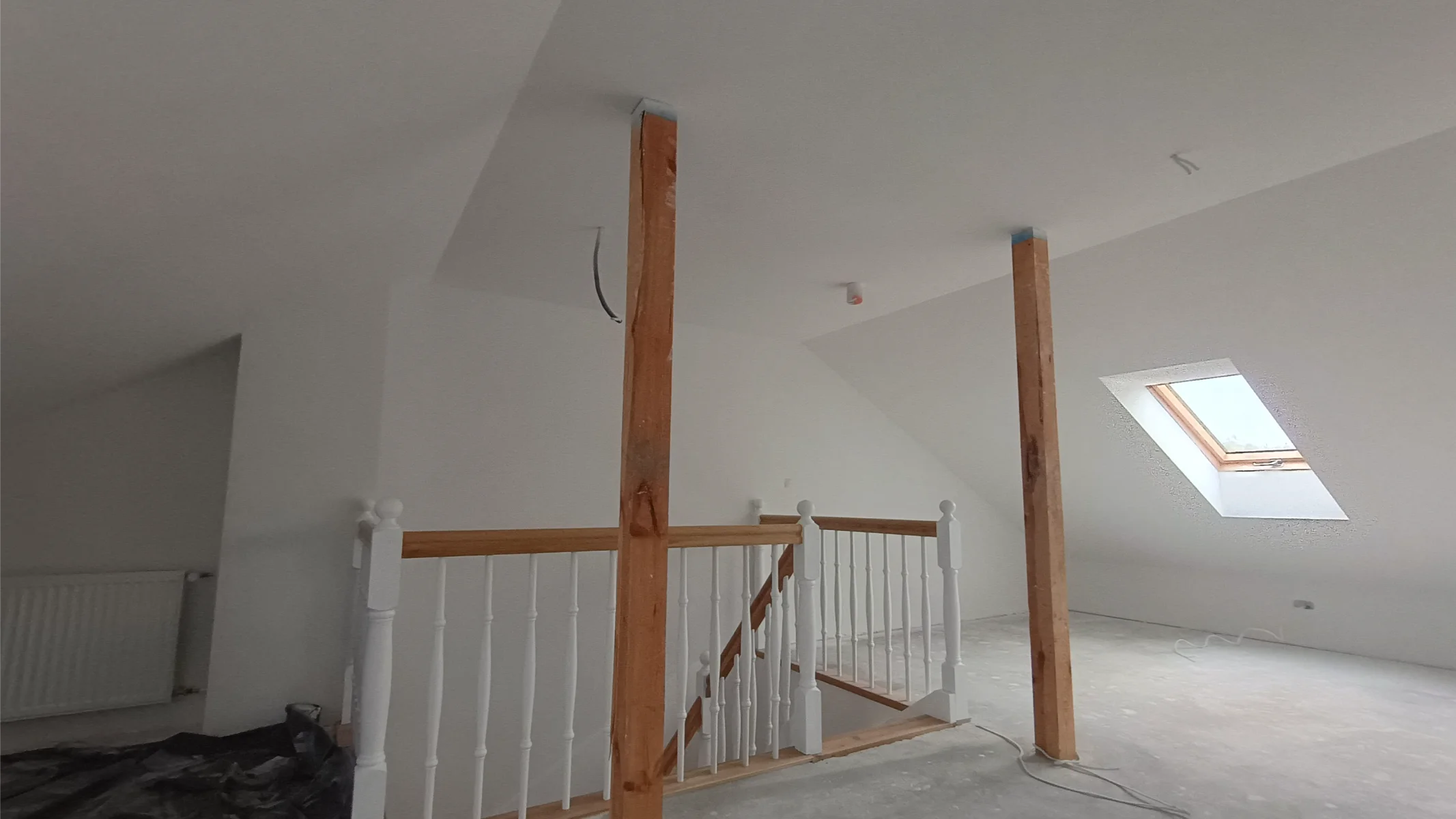 Zabudowa poddasza z gładkimi białymi ścianami, drewnianymi słupami i balustradą