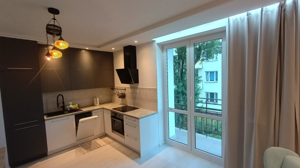 Remont kuchni w nowoczesnym stylu z czarnymi i białymi szafkami, zabudowanym sprzętem AGD, podświetleniem i dużym oknem balkonowym