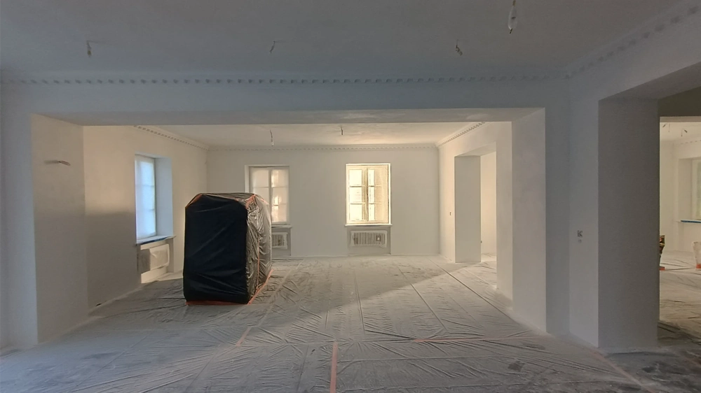 Zagruntowane ściany i zabezpieczona folią podłoga w otwartym wnętrzu gotowym do malowania