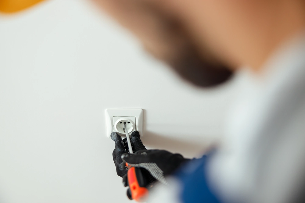 Elektryka – montaż gniazdka elektrycznego przy użyciu śrubokręta na białej ścianie